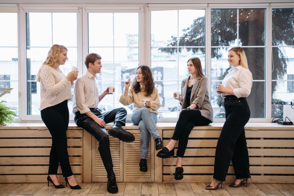 A group of five employees chat together and drink coffee.