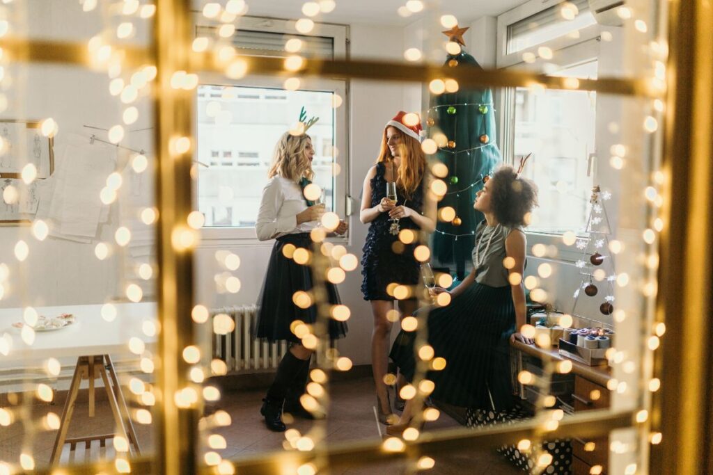 Three professionals sit in a meeting room. The room is decorated for Christmas with fairy lights