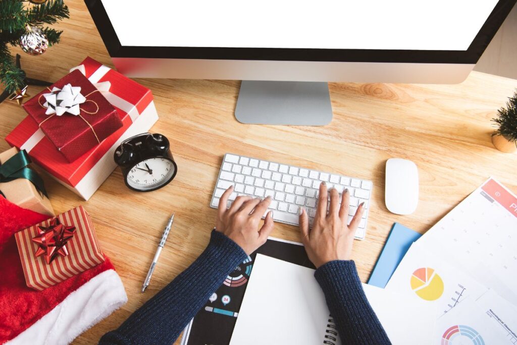An employee works at their computer, there are Christmas gifts on their desk beside them.