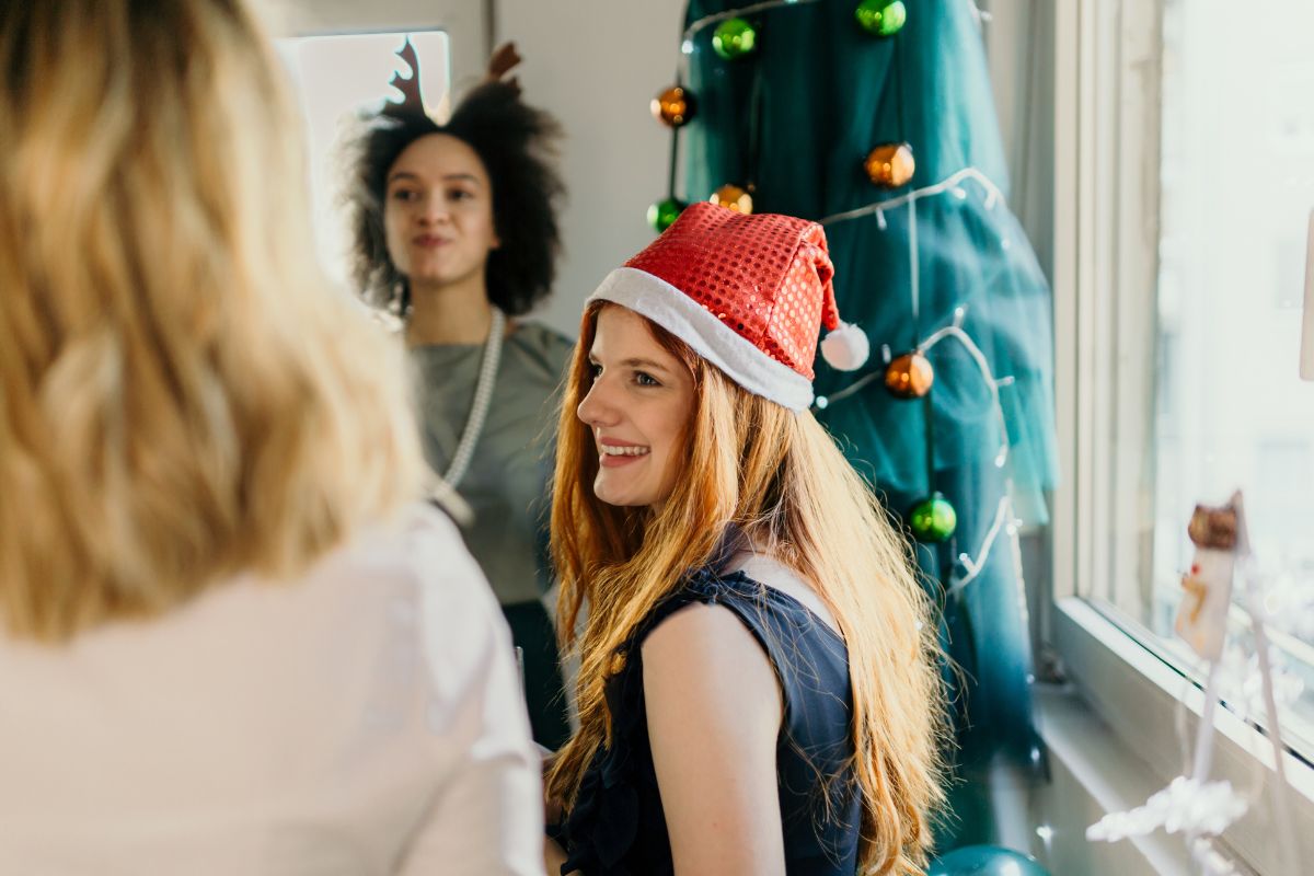 Three women take part in a meeting, they are wearing Santa hats. There is a Christmas tree in the background.