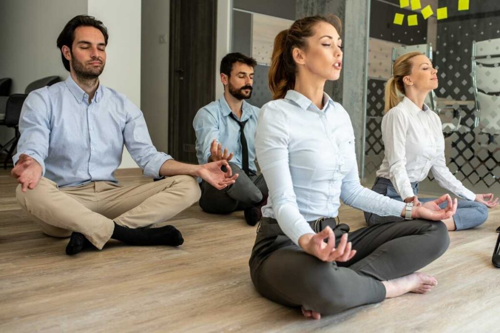 group of office workers sitting cross legged and meditating on the floor