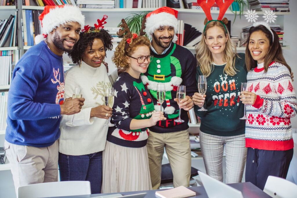 festive group picture of colleagues in the office, smiling and wearing Christmas jumpers and drinking champagne. 