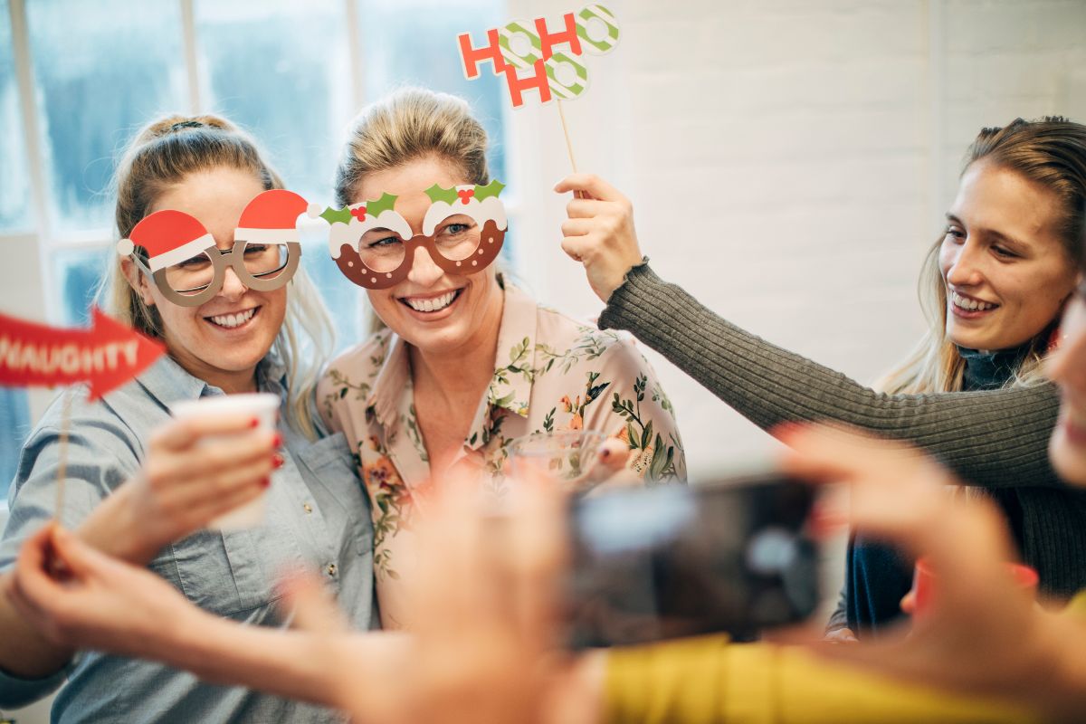 group of office workers pose for a festive photo, wearing funny Christmas glasses and holding Christmas props