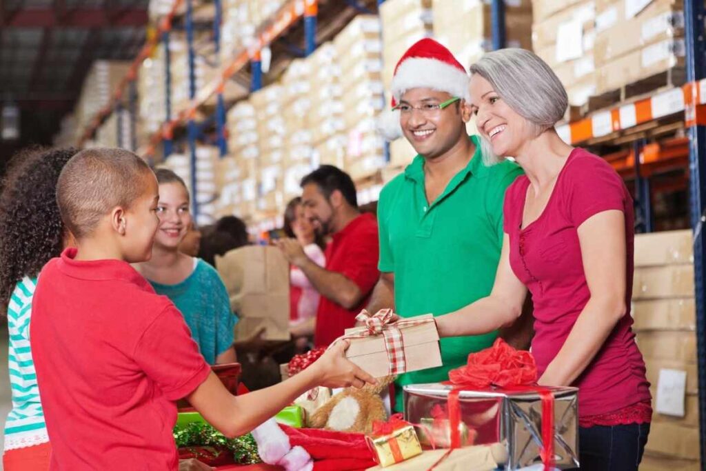 a festive picture of people helping at a Christmas charity event, handing wrapped presents to a group of children. 