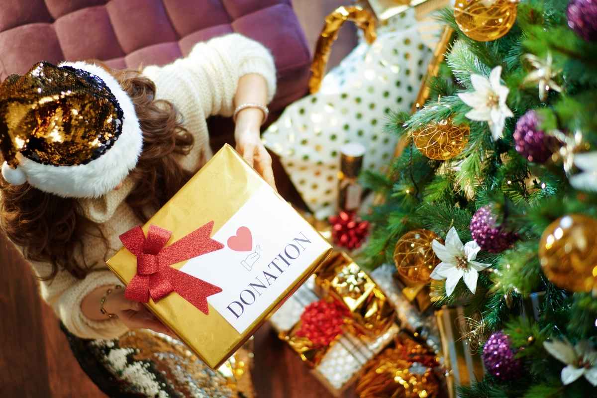 women in Santa hat holds charity donation box by Christmas tree