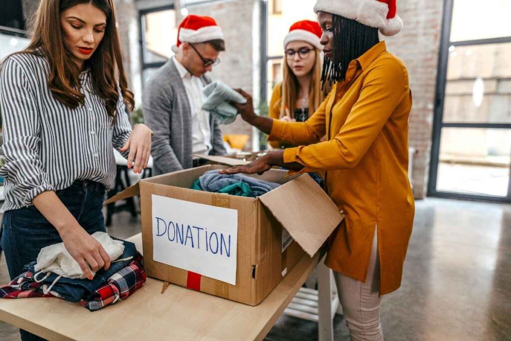 group of colleagues fill a donation box with clothes. they all wear santa hats.