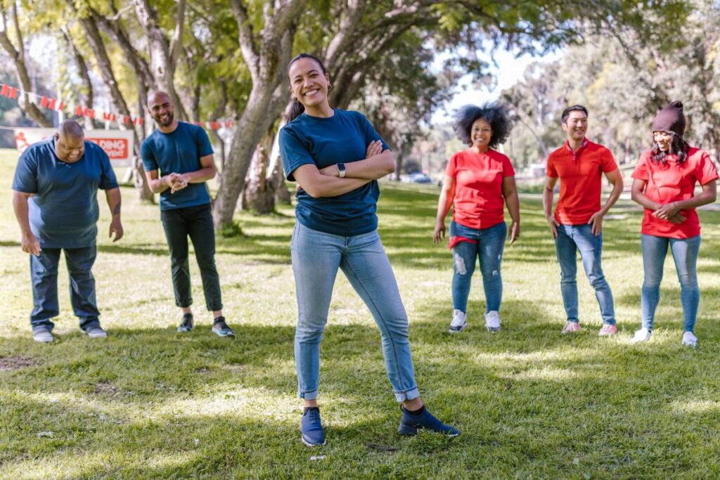 a group of 6 co-workers in blue and red shirts do team building activities in a park.