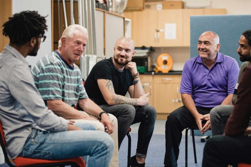 circle of 6 men, all of different ages and races, smiling as they talk with each other 