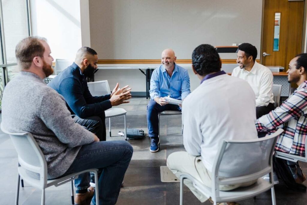 seminar of 6 men of different ages and races in formal workwear, talking and smiling. 