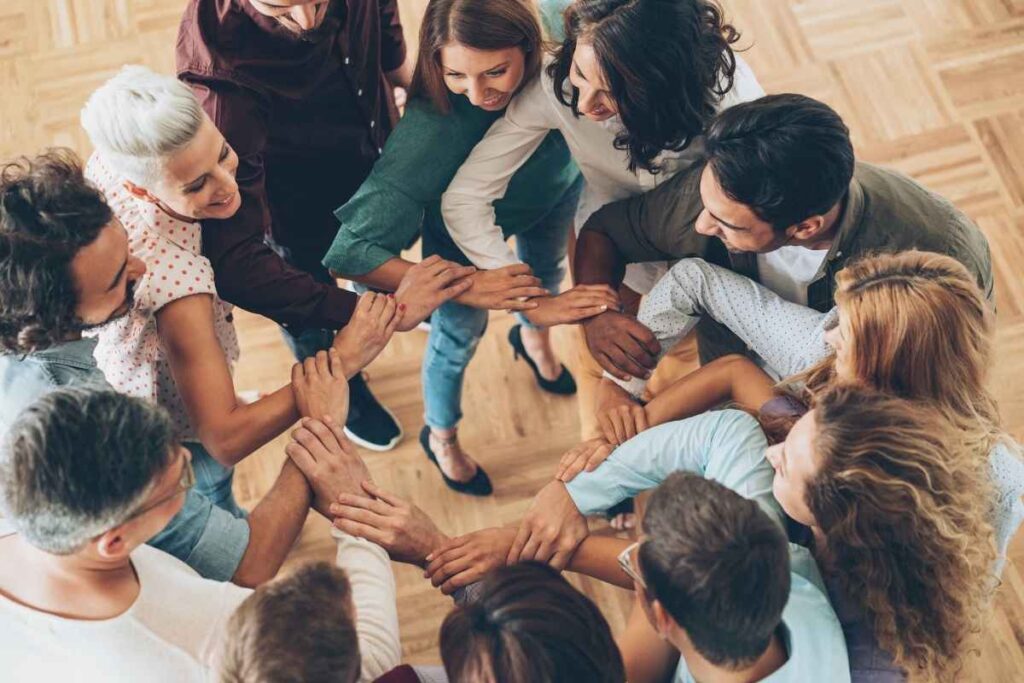 A group of smiling adults stand in a circle holding hands.