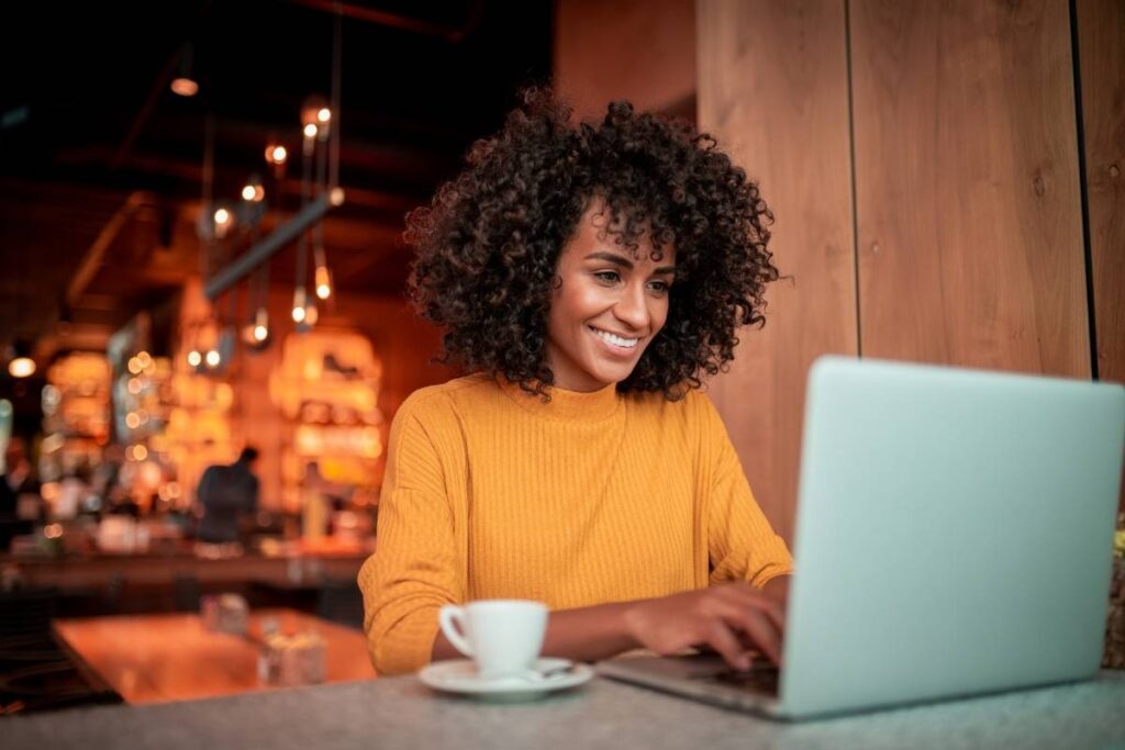 a smiling woman sits in a café on her laptop. 