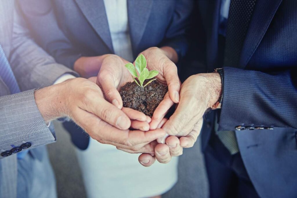 three people dressed in suits stand in a circle and hold soil with a plant growing from it. 