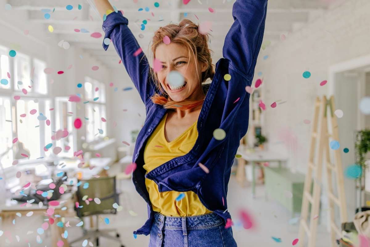 a woman celebrates as confetti falls around her. she is in an office or studio