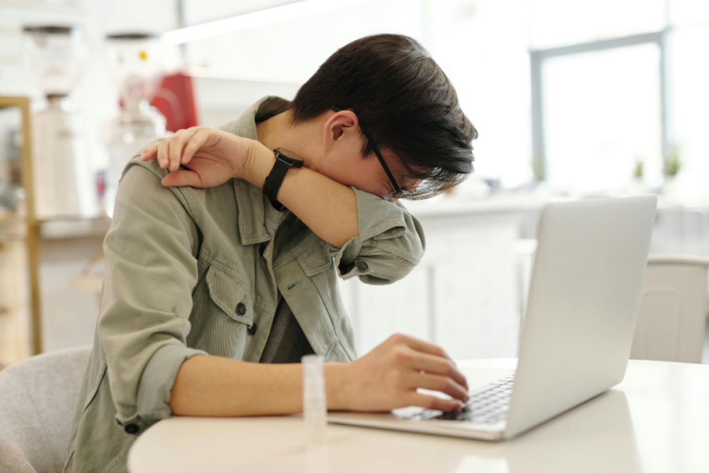 A man sits at his desk and sneezes into his elbow.