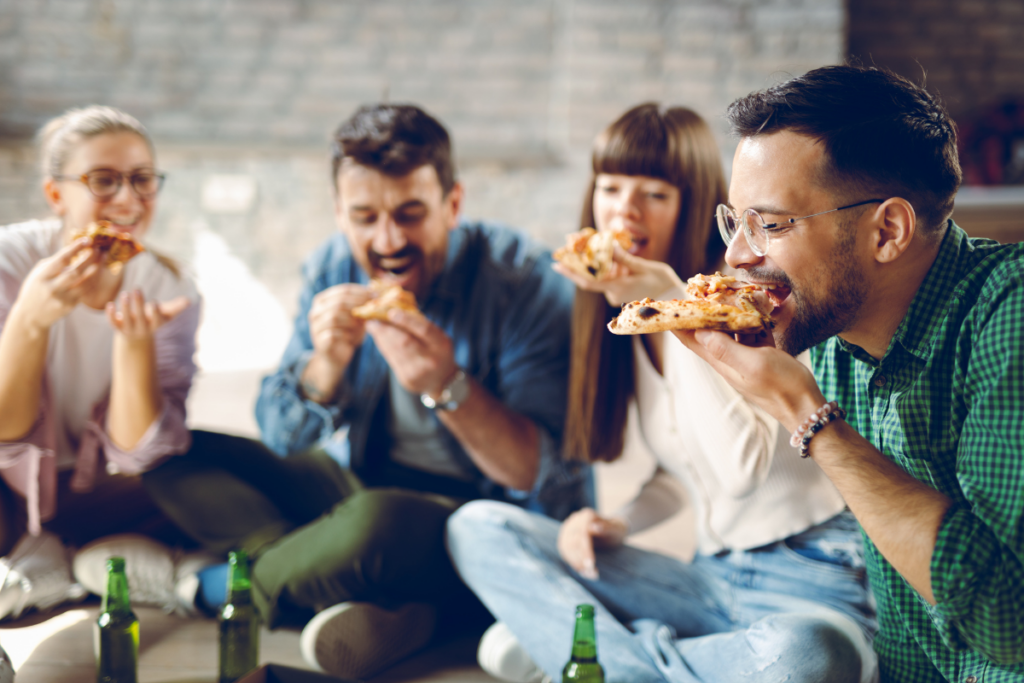 a group of people sit cross legged on the floor and eat pizza together. 