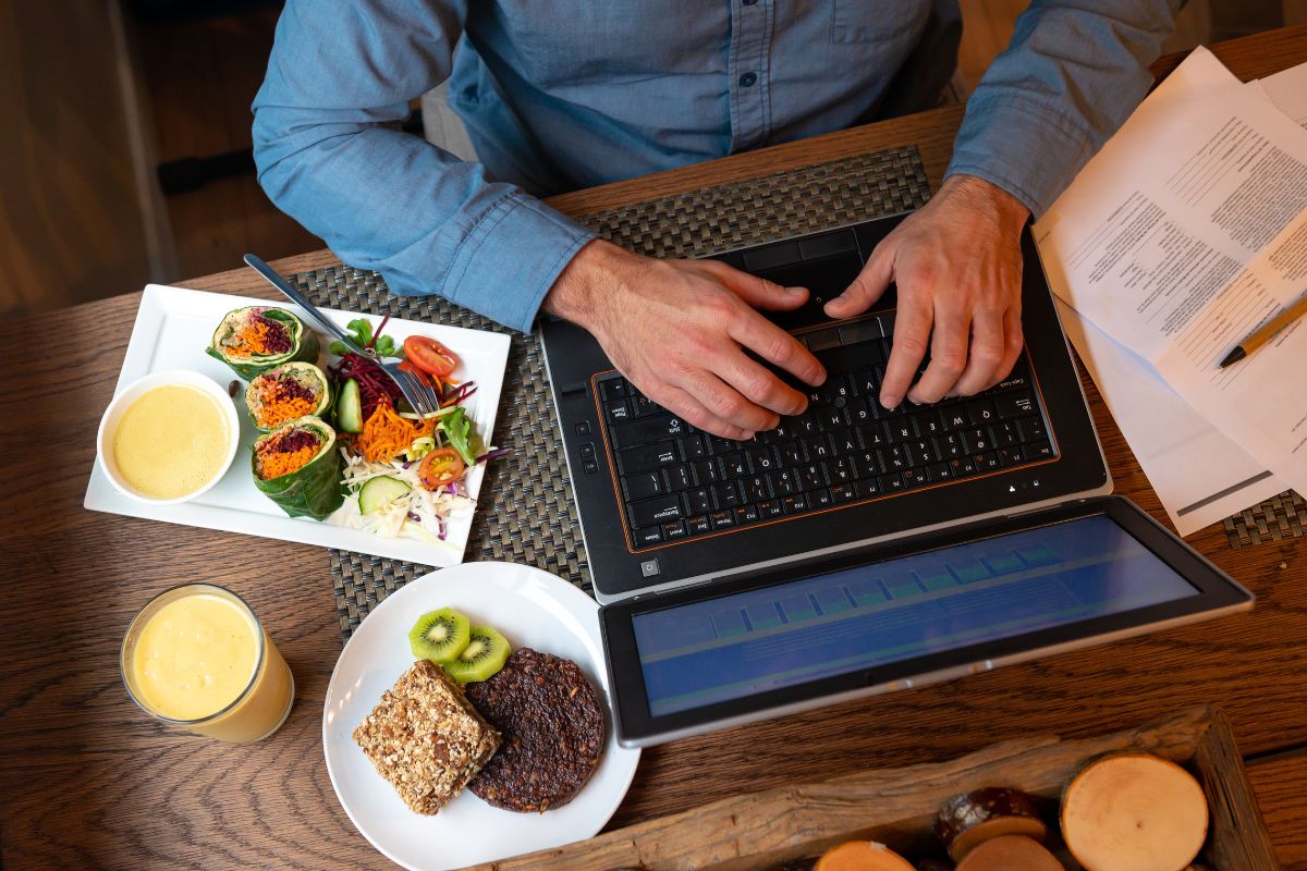 A man sits at his laptop next to plates of healthy food and a smoothie