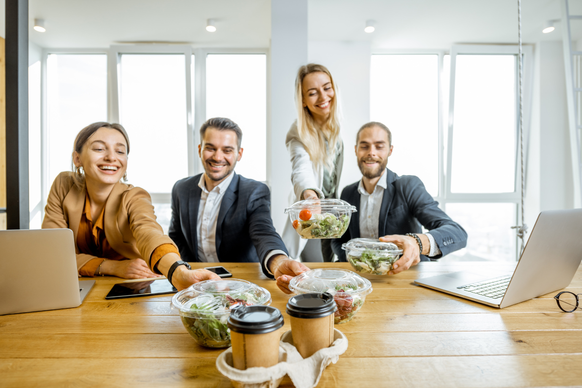 A group of colleagues reach for salads and coffee. They are smiling.