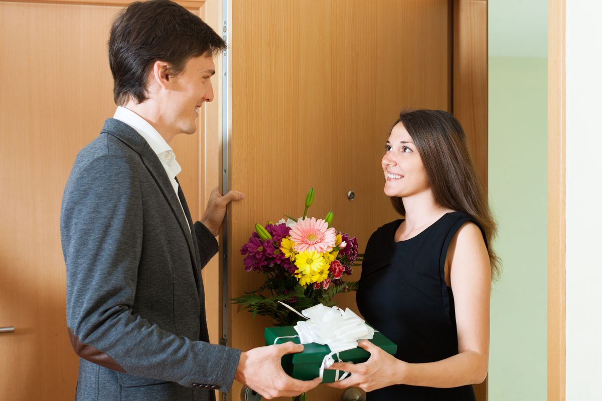 A man passes a women flowers and a wrapped gift. They are both smiling