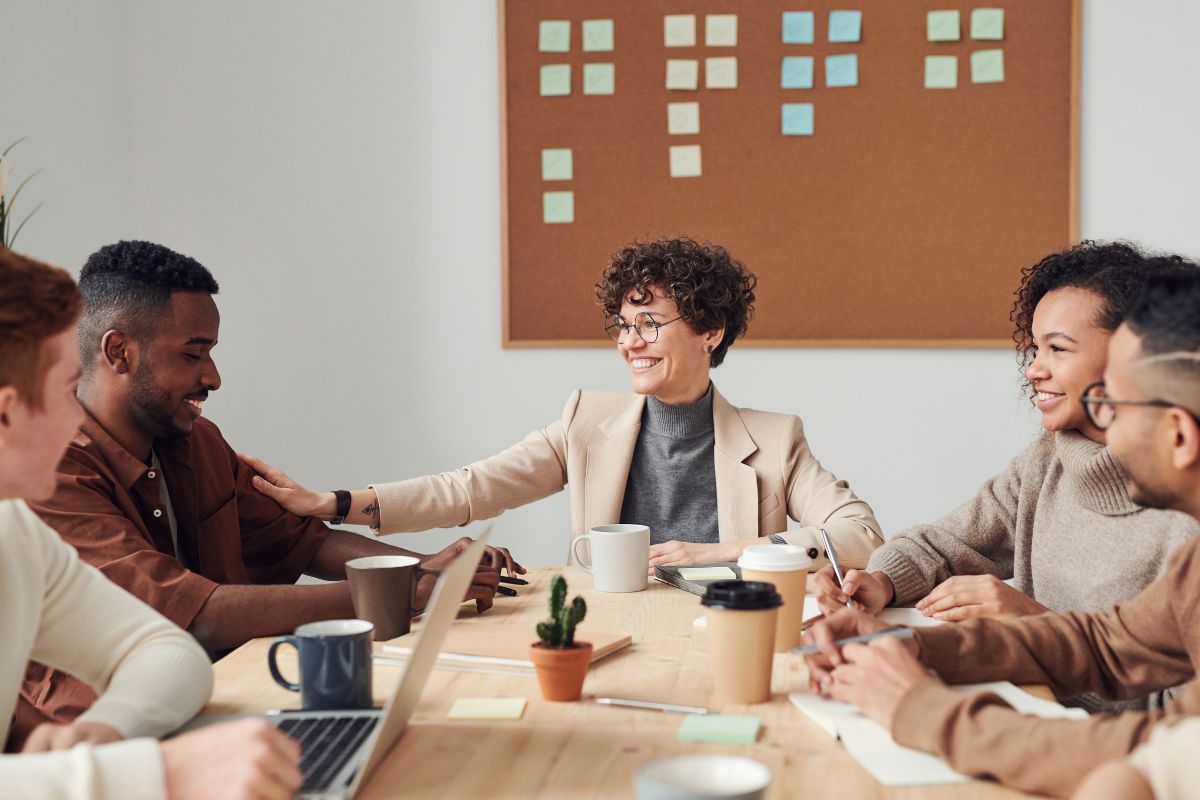 a group of coworkers sit around a table, smiling and chatting.