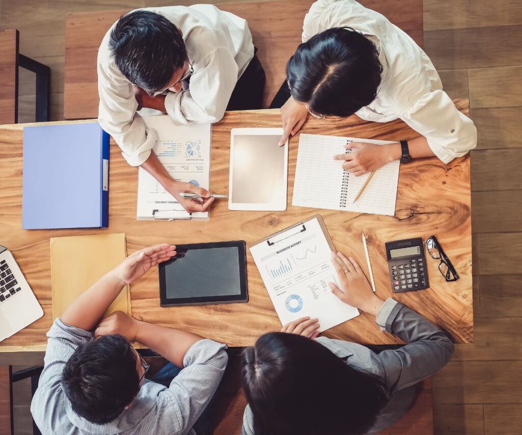 a group of colleagues work together on a budget. There are tablets and calculators on the desk