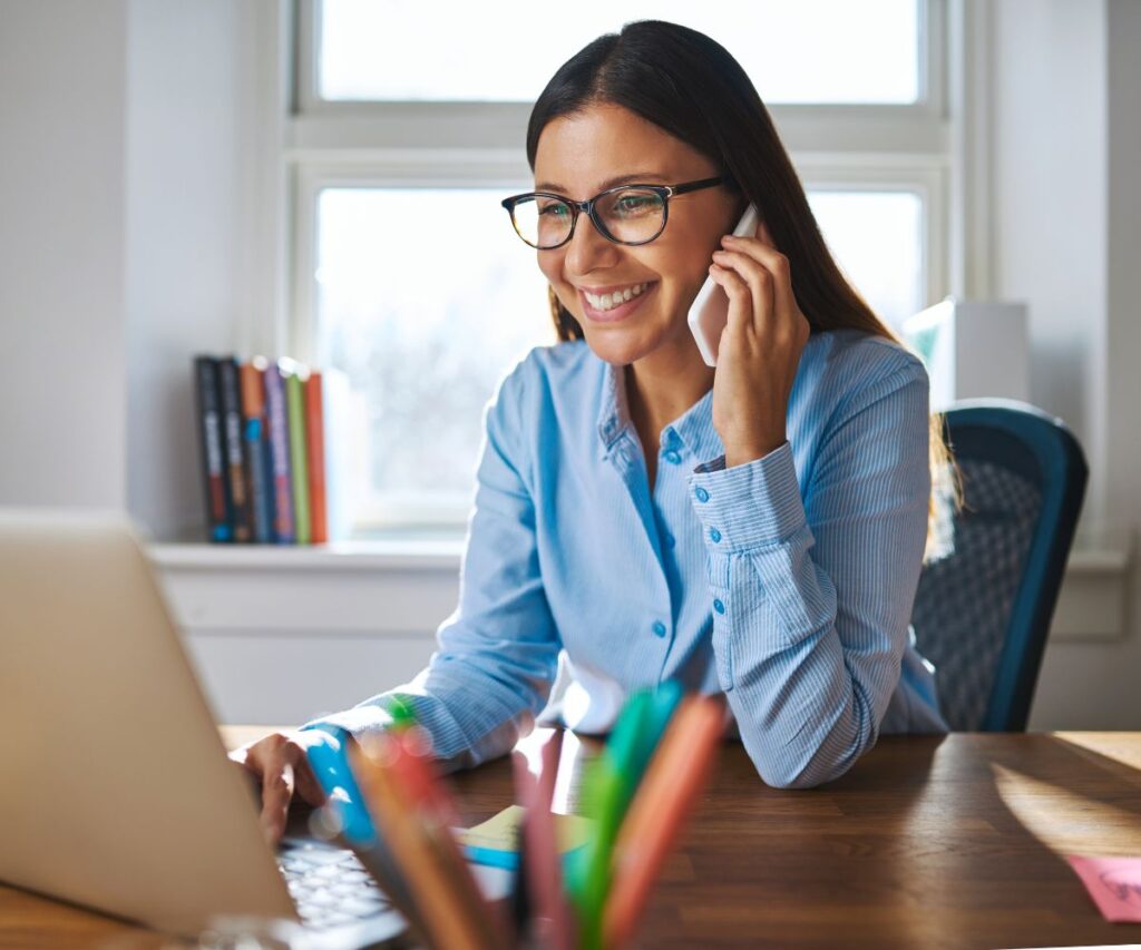 a woman smiles whilst sat at her desk and talking on the phone