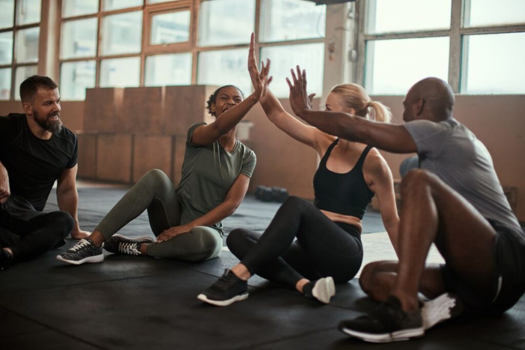 A group of four co-workers sit on the floor of a yoga studio and high-five.