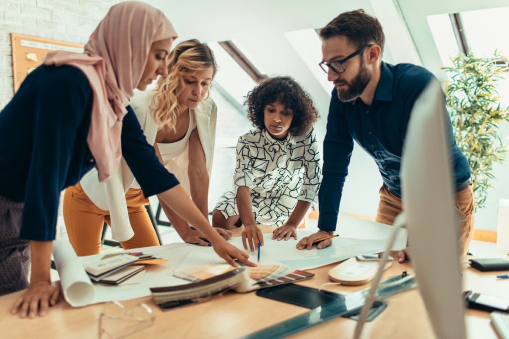 A group of colleagues stand over a table together and work on a blueprint.