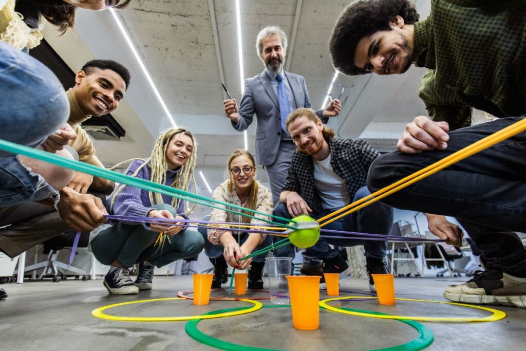 A team of co workers take part in team building activities involving plastic cups and a tennis ball.