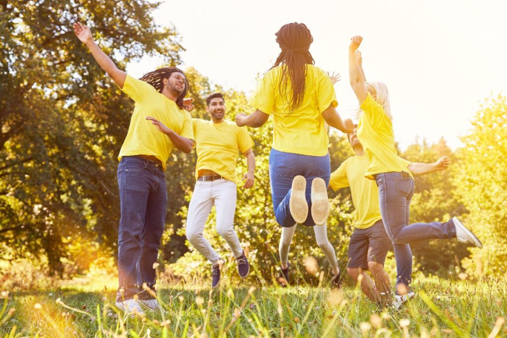 A group of team members jump up in celebration. They are doing team building activities outside.
