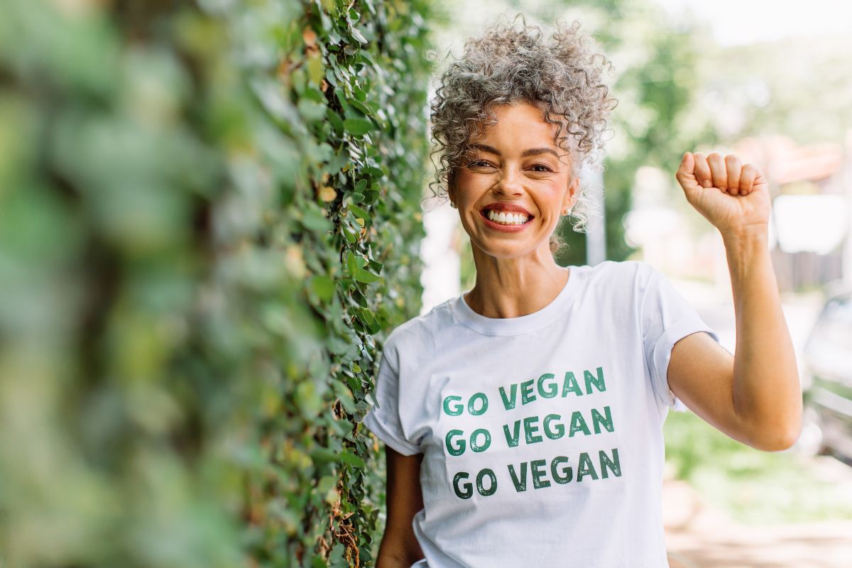 A woman holds her fist up and smiles. She is wearing a 'Go Vegan' t-shirt