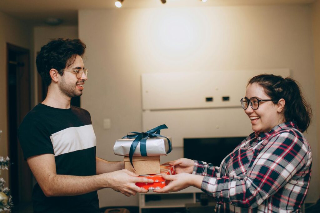 Two colleagues exchange a pile of gifts. They are both smiling.