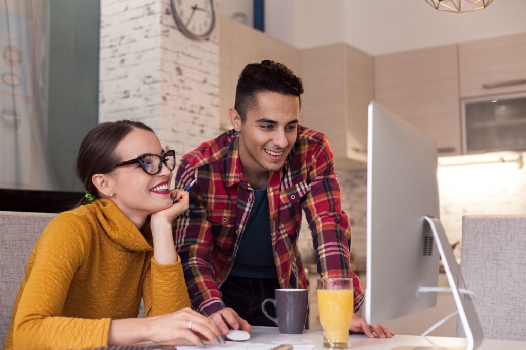 Two professionals work together on a computer. They are both smiling.