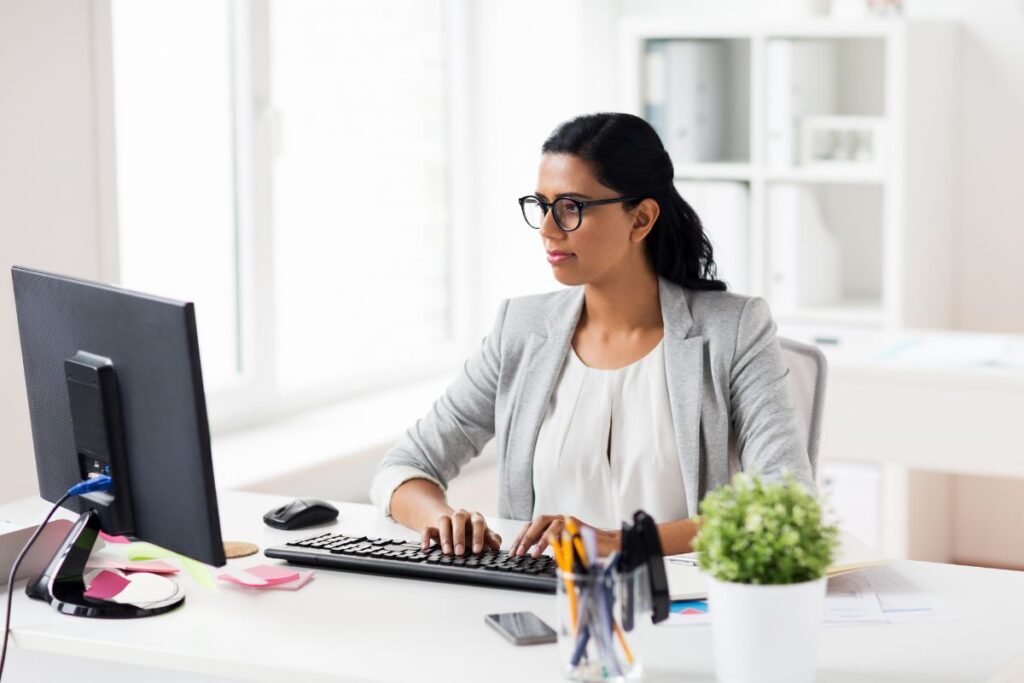 A woman sits on her computer at work. She wears formal workwear.