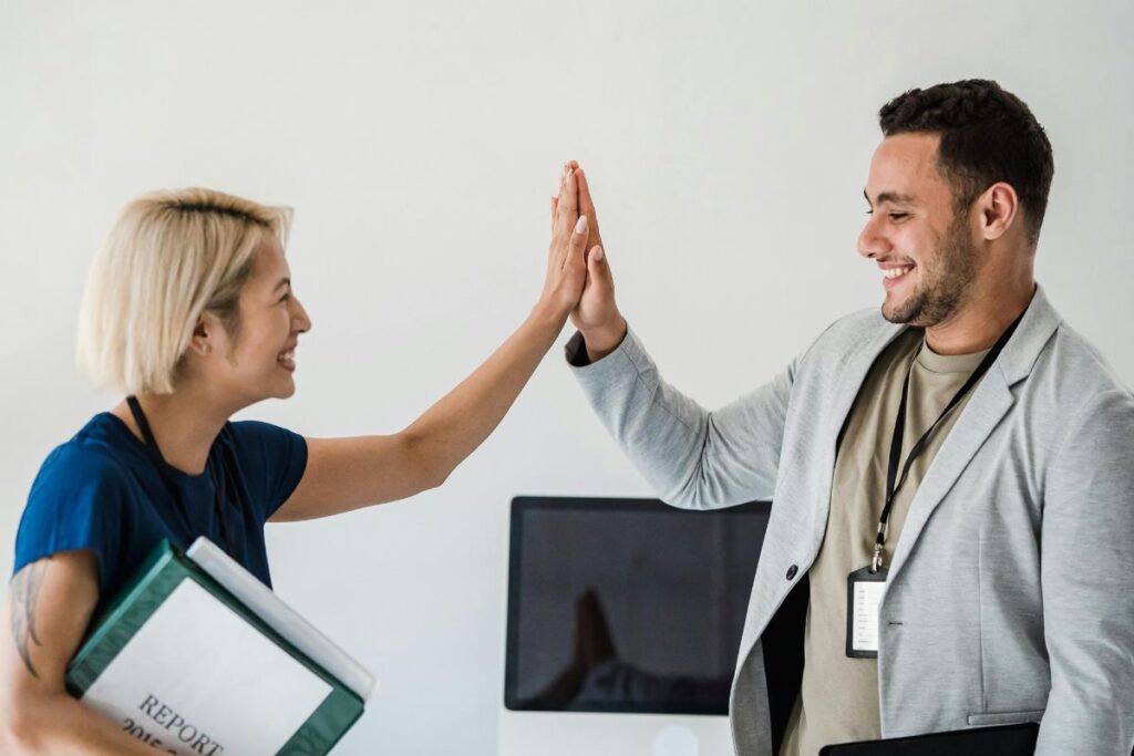 A woman high fives a man in the workplace. They are both smiling