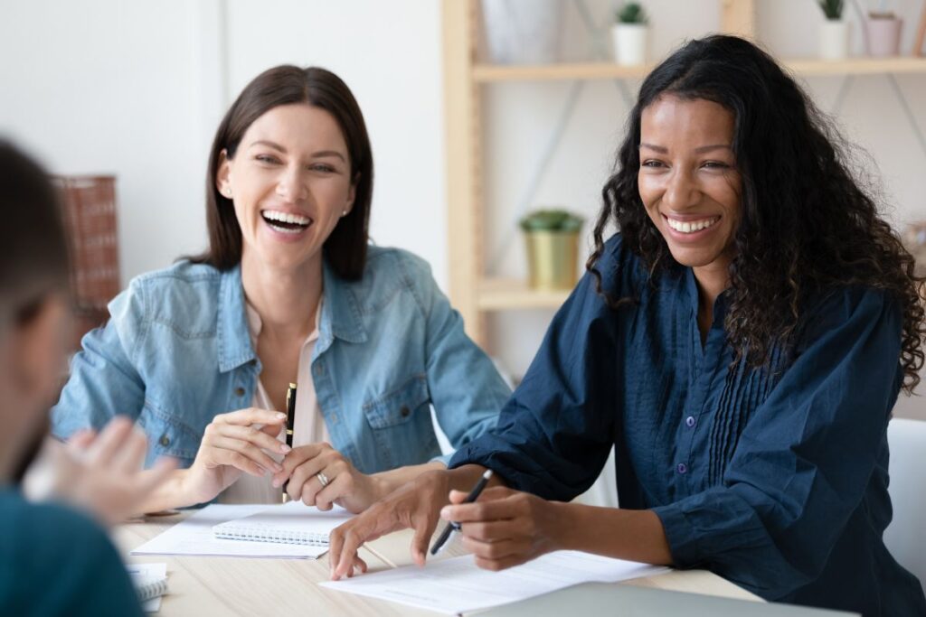 Two women smile and laugh together in a work meeting.