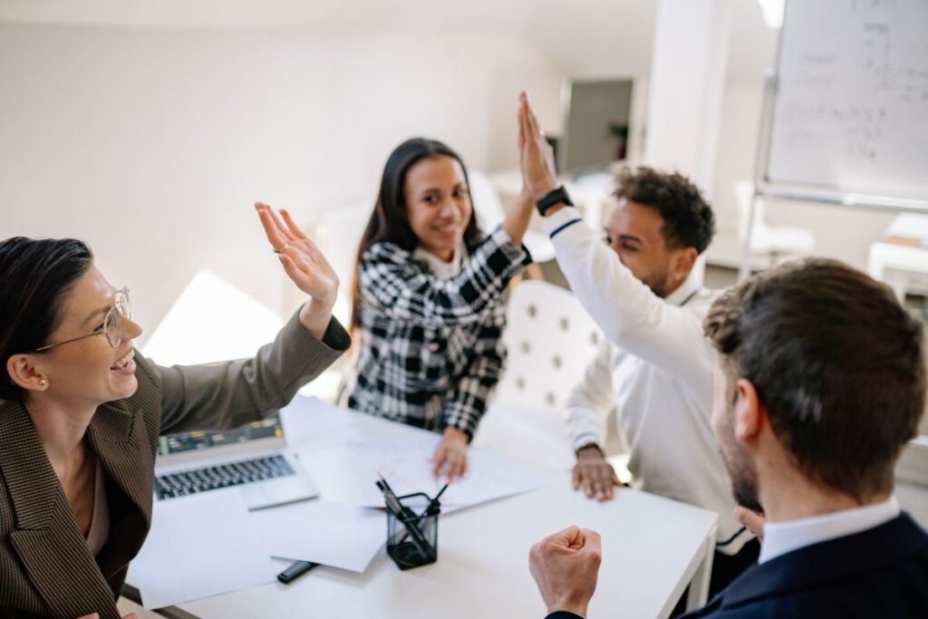 A group of four professionals high five each other in a meeting room.