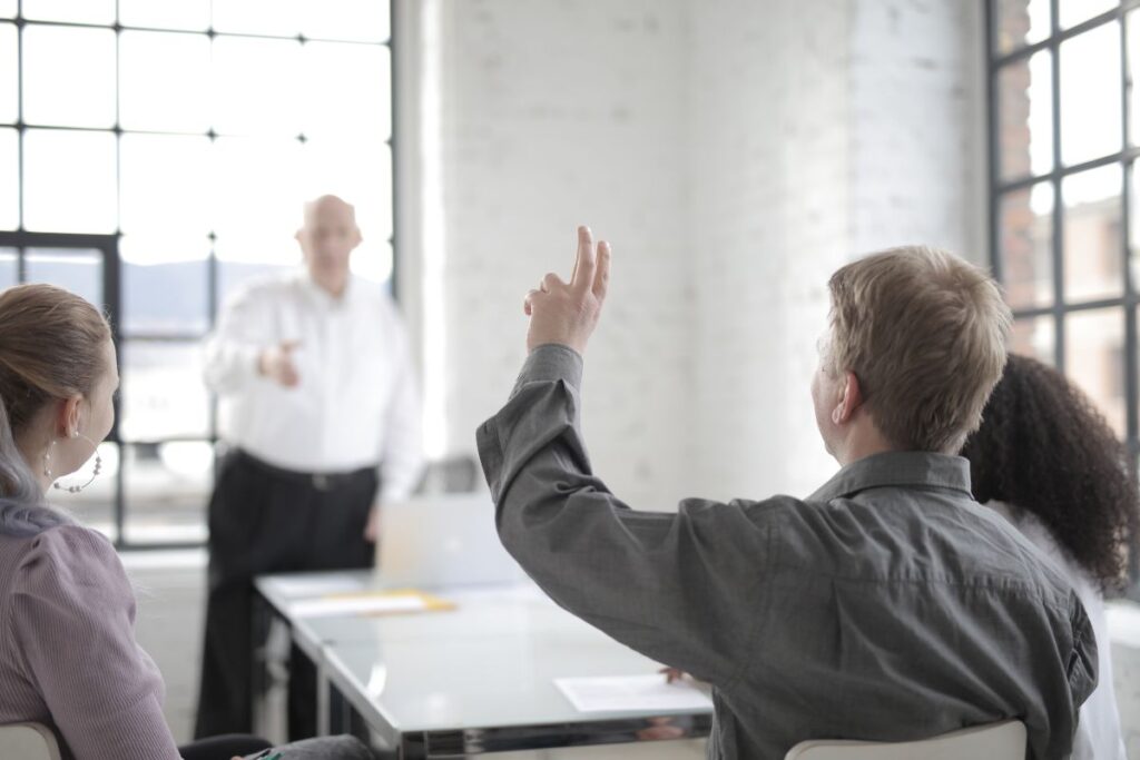 A man puts his hand up in a meeting to ask a question to a manager.