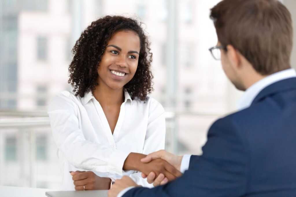 A woman smiles and shakes hands with her interviewer.