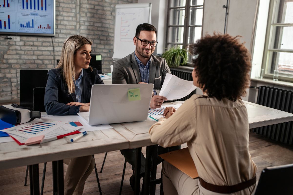 A woman sits in an interview, opposite a man and a woman. The man is smiling.