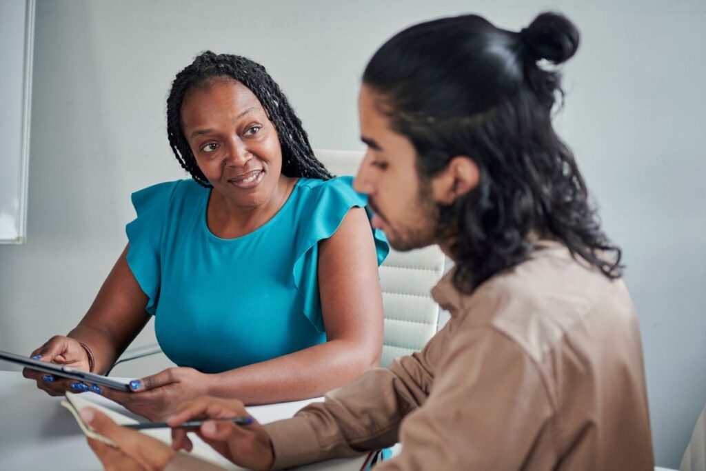Two employees sit in a feedback meeting together.