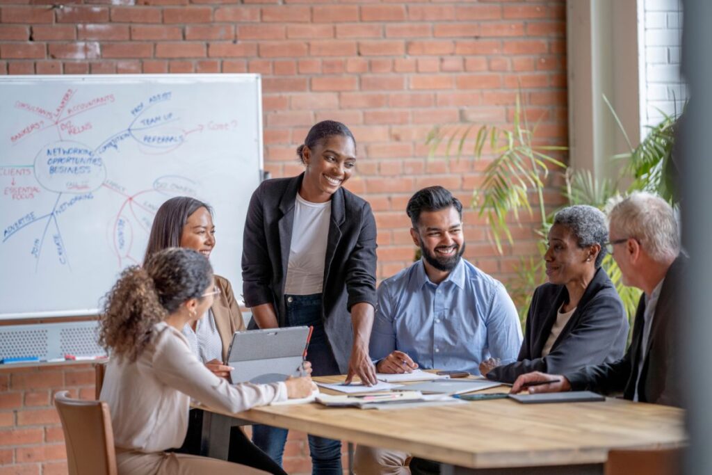 A group of happy employees sit together in a meeting. They brainstorm together.