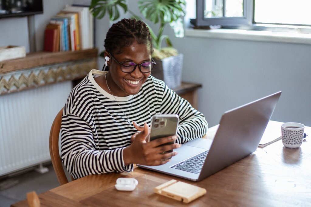 A woman works from home. She smiles at her phone at her desk.