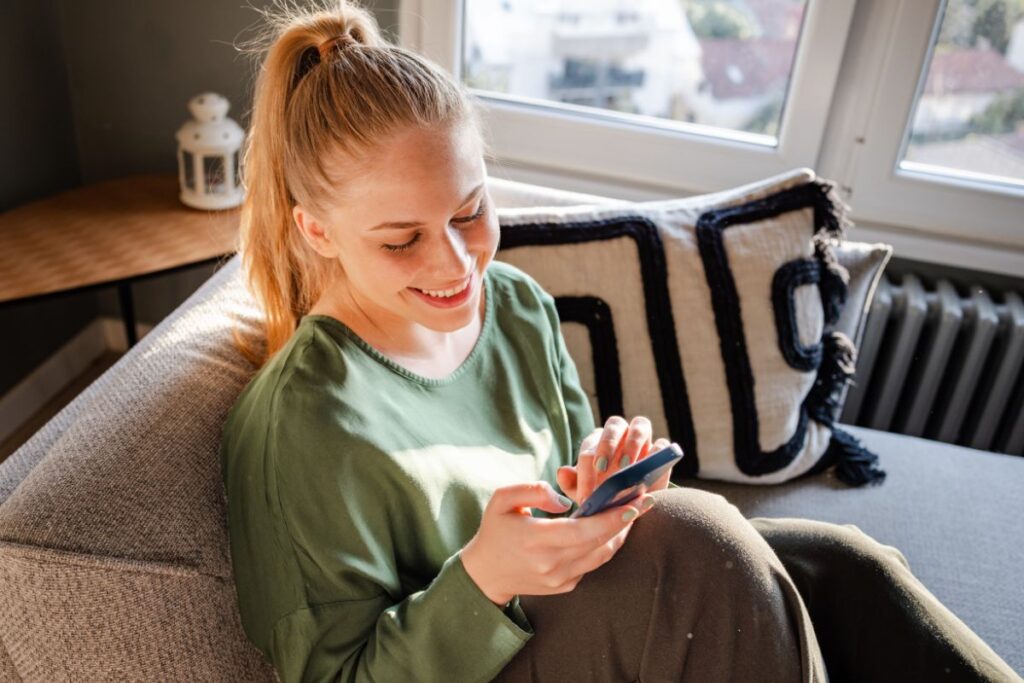 A woman scrolls on her phone and smiles.