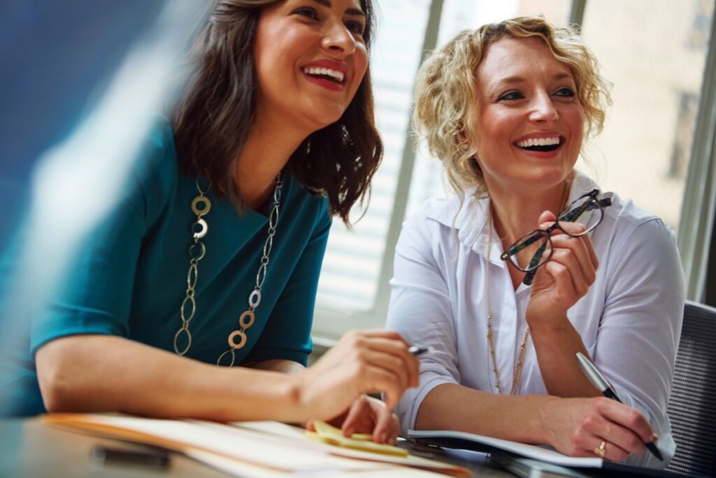 Two female employees sit together in a meeting and smile.