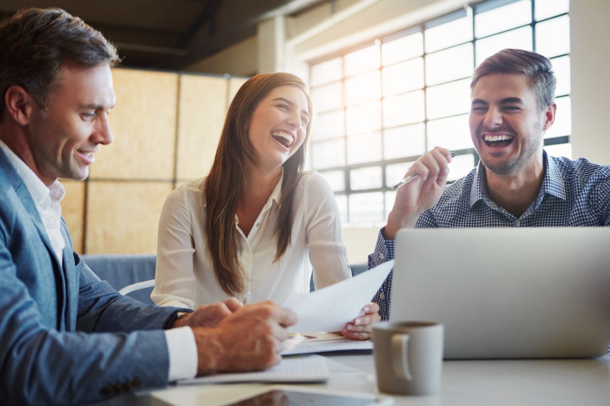 A group of three employees work together on a project. They are all laughing with each other.