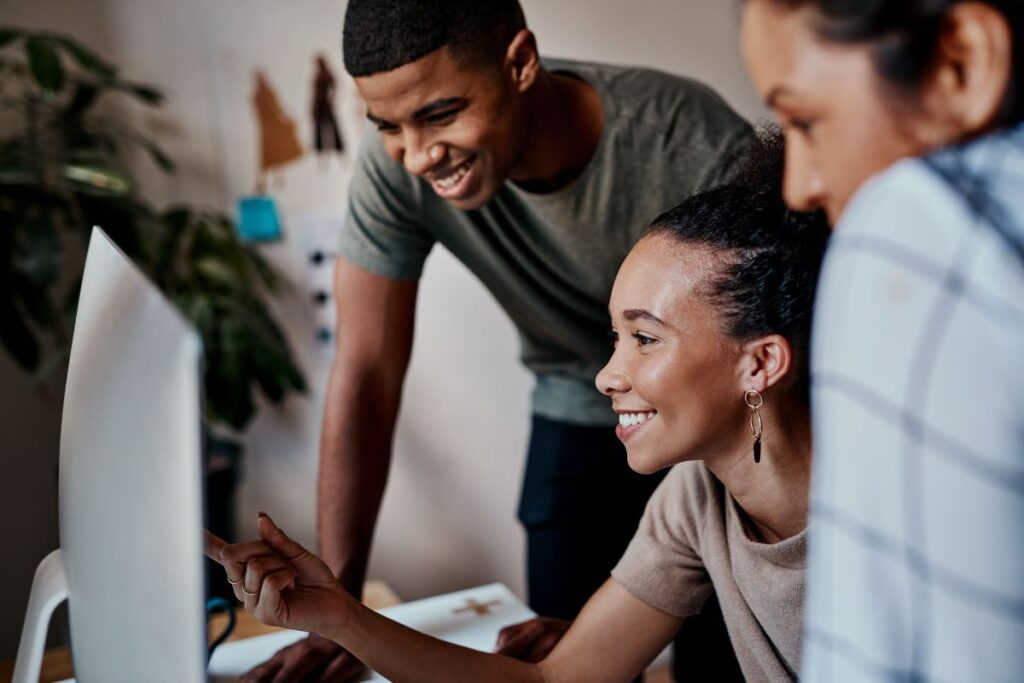 A group of three colleagues sit together and work on a project on a computer.