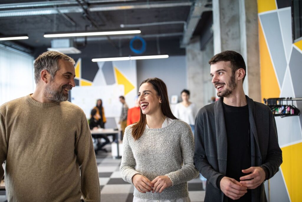 Three colleagues walk through an office space together. They smile and laugh together.