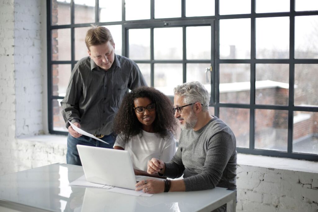 Three colleagues sit in a meeting together and collaborate in front of a laptop screen.