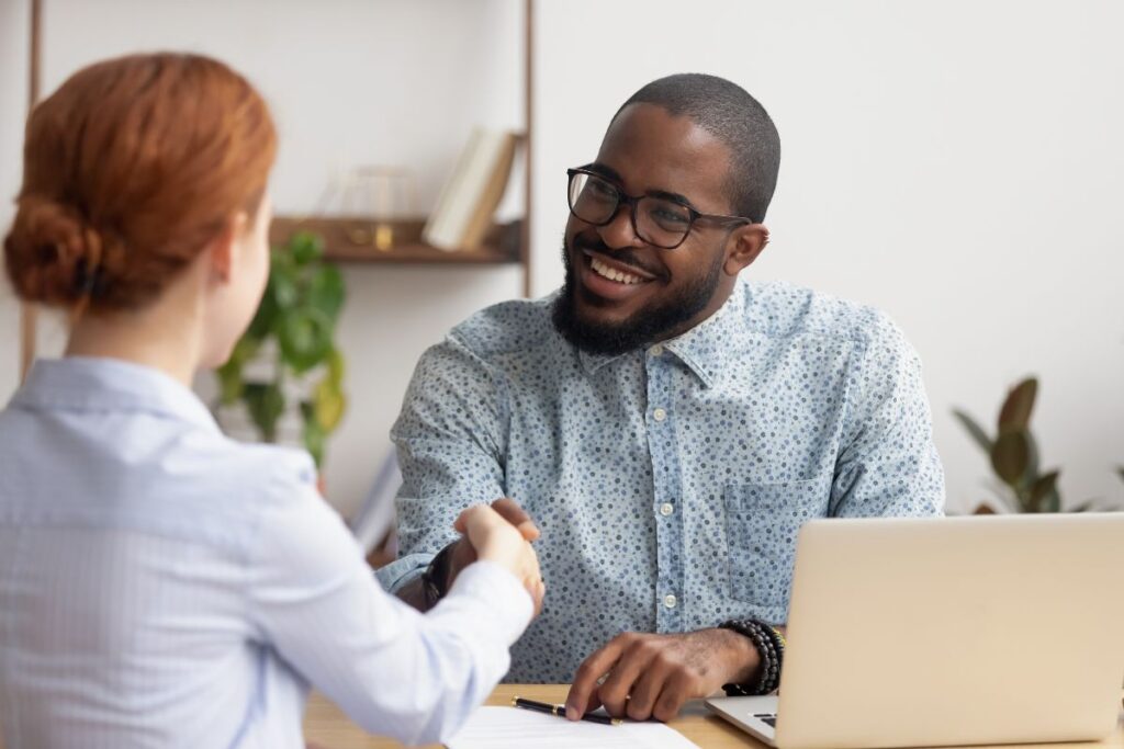 A man smiles and shakes hands with a woman in an interview setting