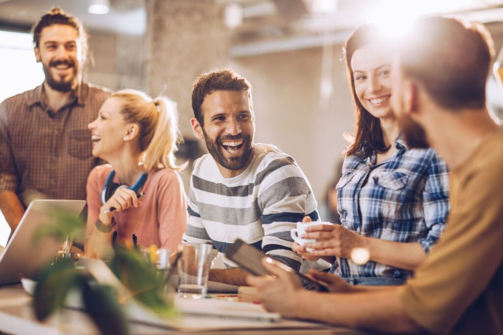 A team laugh and drink coffee together as they take a meeting
